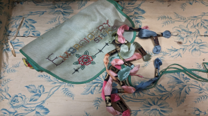 A silk Embroidery set from the collection of Miss Ena Lynn. A green silk pouch with the hand embroidered word 'embrodery' and a small collection of multi coloured silk thread.